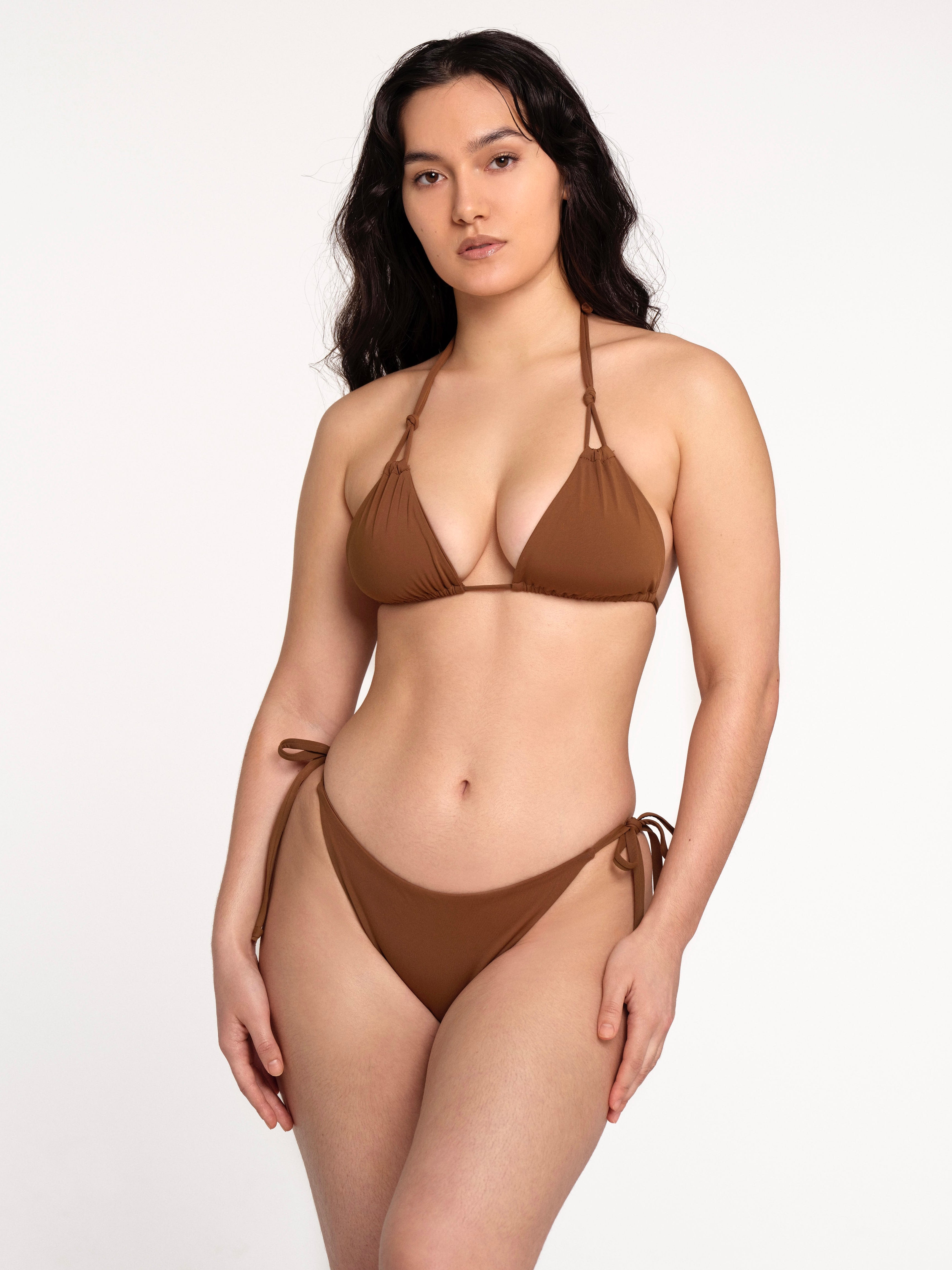 Woman wearing the Kaiserin Delma Top – Cinnamon, a brown triangle bikini top with double strap halter neck and adjustable sliding cups, styled with matching side-tie bikini bottoms against a plain studio background.