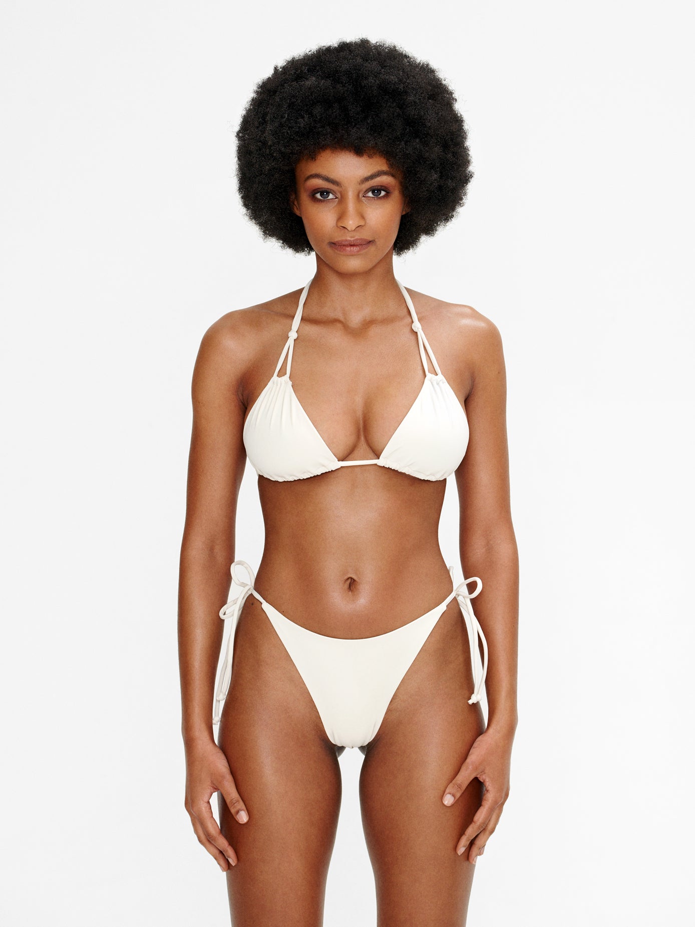 Model wearing the Kaiserin Nona Bottom – Cream, featuring adjustable side ties and a mid-rise fit, shown with a matching cream bikini top for a minimalist and balanced swimwear look.